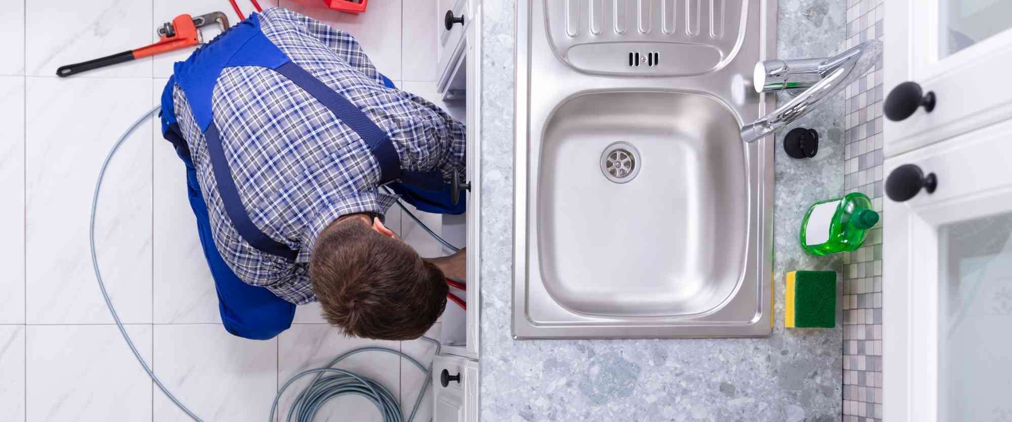 Young Male Plumber Cleaning Clogged Sink Pipe In Kitchen